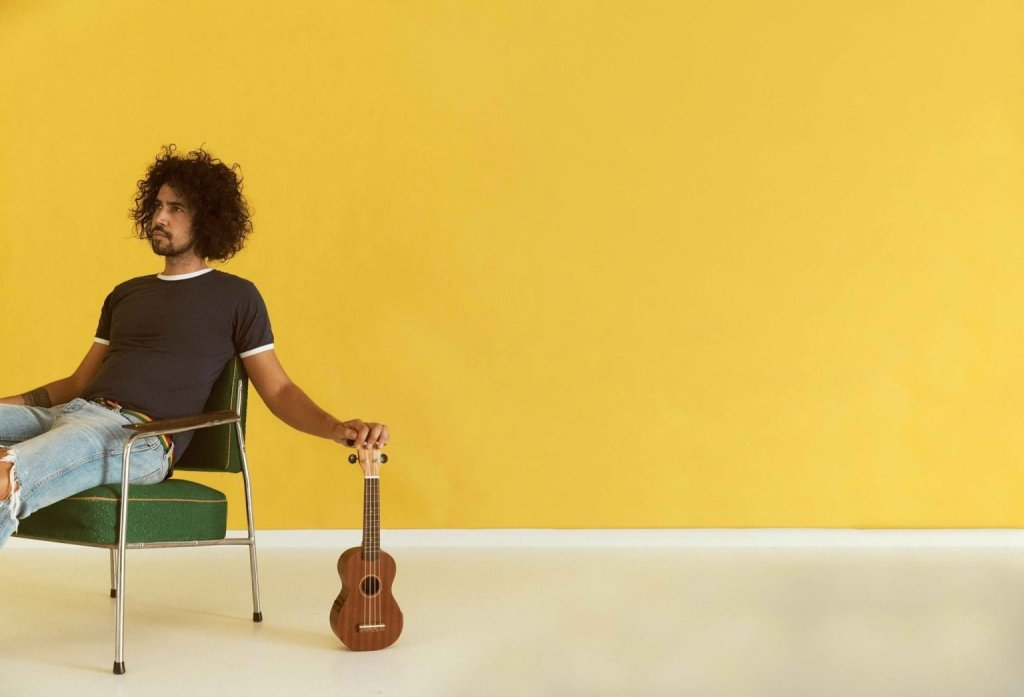 A man with curly hair sits on a green chair holding a small ukulele in Central Oregon.