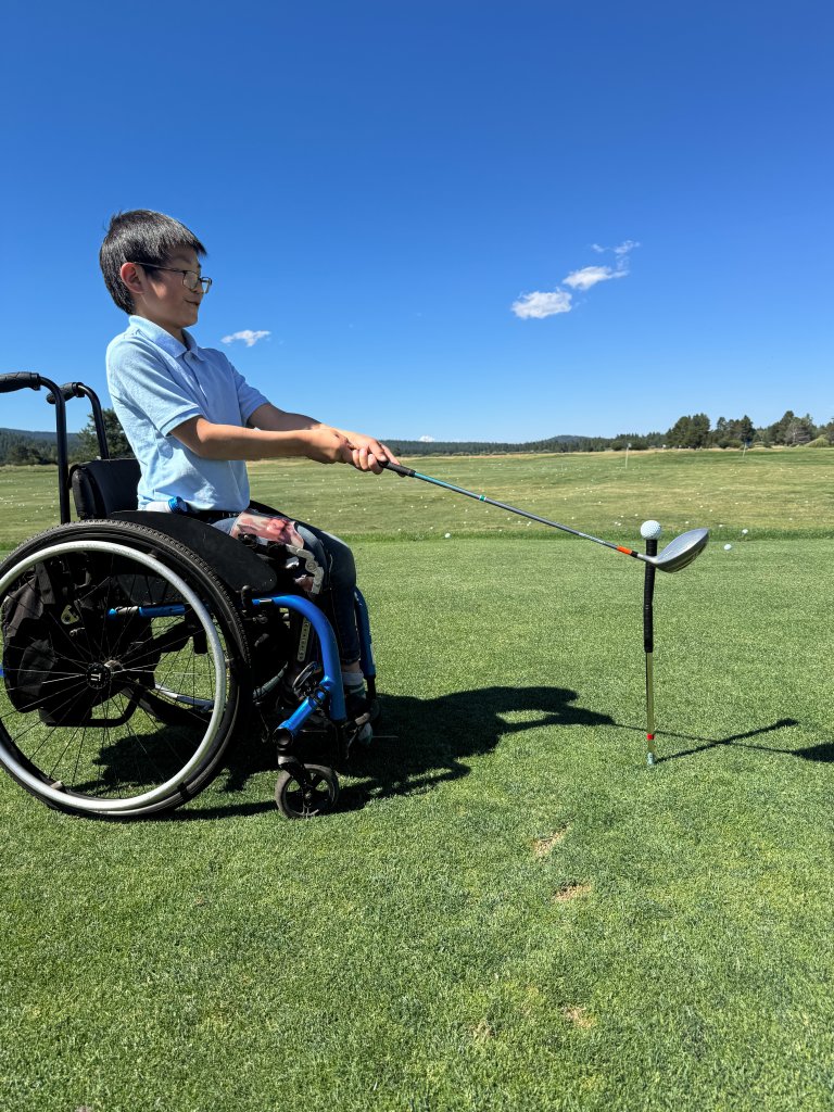 A young boy in a wheelchair prepares to hit a golf ball on a course in Central Oregon.