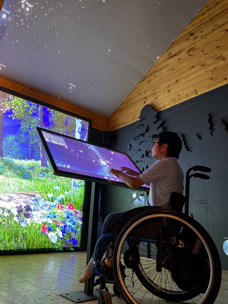 A child in a wheelchair interacts with a digital star map display in Central Oregon.