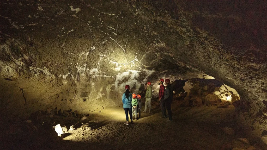 A group of people wearing hard hats explore a dimly lit cave in Central Oregon.