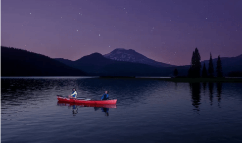 Two people in a red canoe on a lake under a starry night sky in Central Oregon.