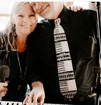 A smiling couple posing together, with the man wearing a piano-themed necktie in Central Oregon.