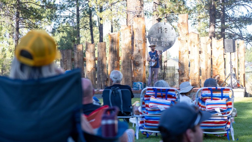 A musician plays a banjo on an outdoor stage for an audience in chairs in Central Oregon.