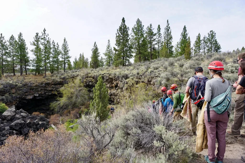 A group of people wearing helmets prepare to explore a rocky cave entrance in Central Oregon.