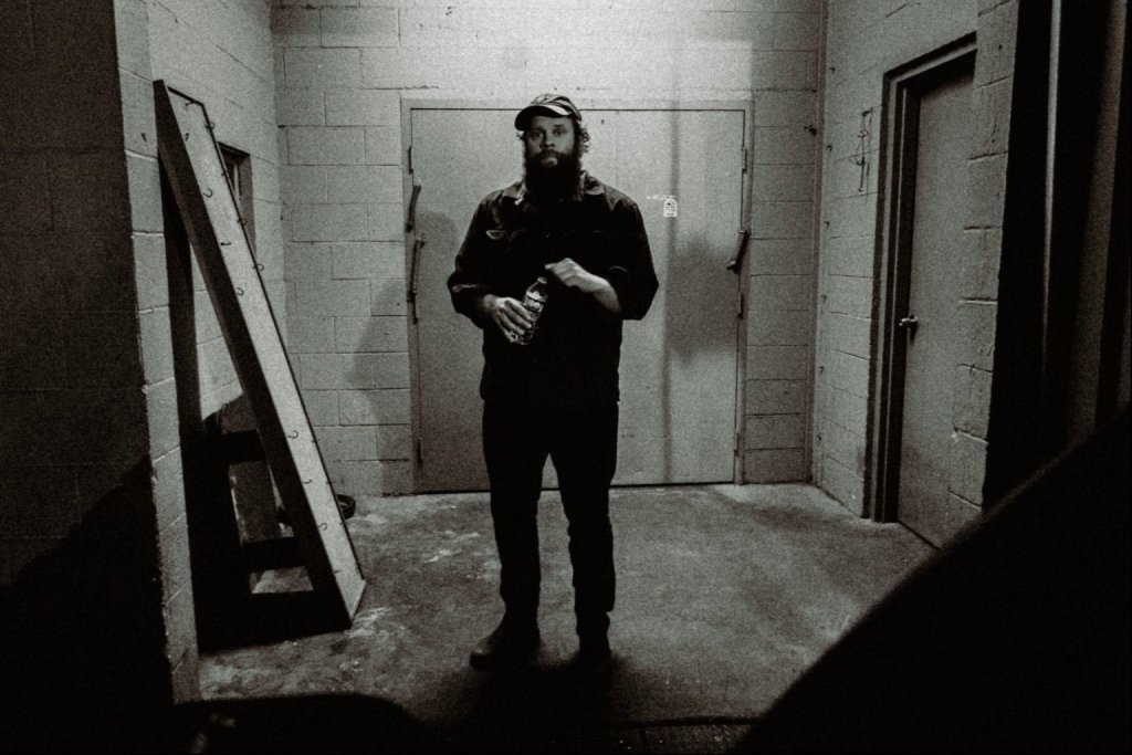 A bearded man in a cap stands in a dimly lit industrial room in Central Oregon.