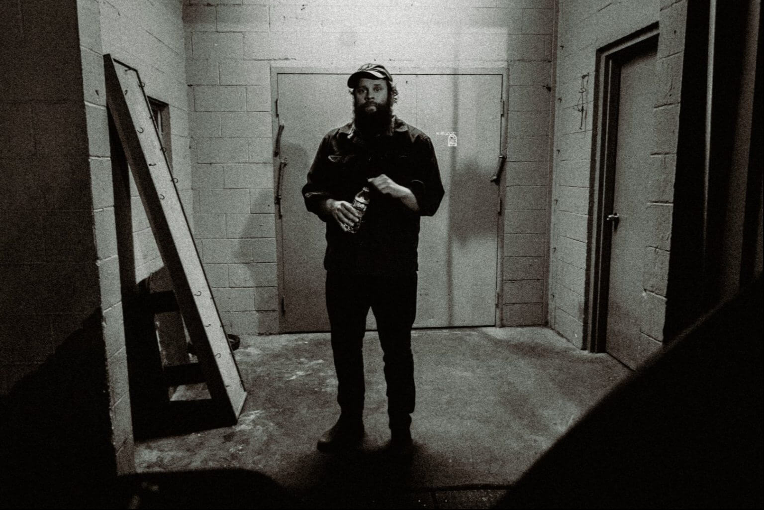 A bearded man in a cap stands in a dimly lit industrial room in Central Oregon.