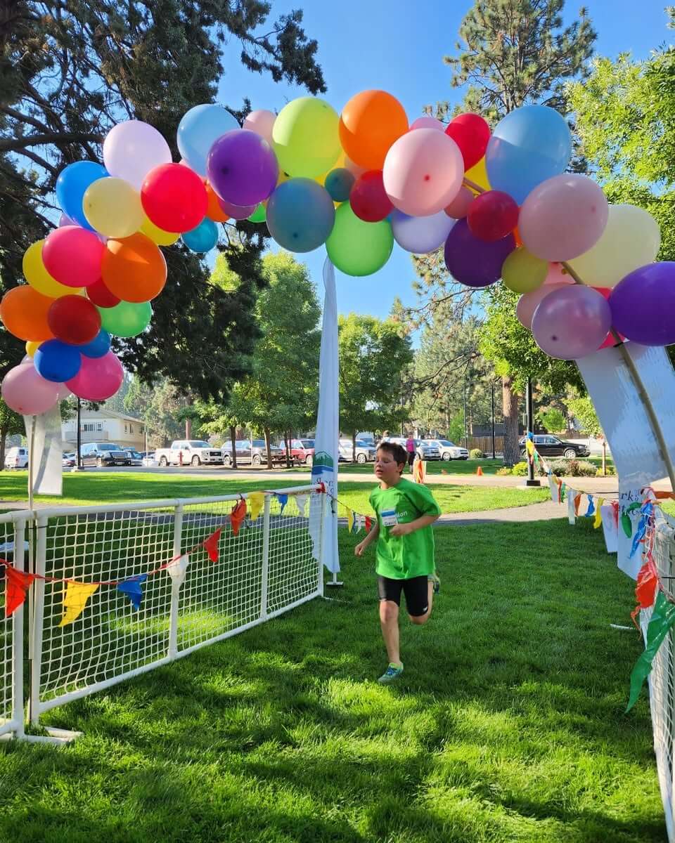 A young boy in a green shirt runs through a colorful balloon archway in Central Oregon.