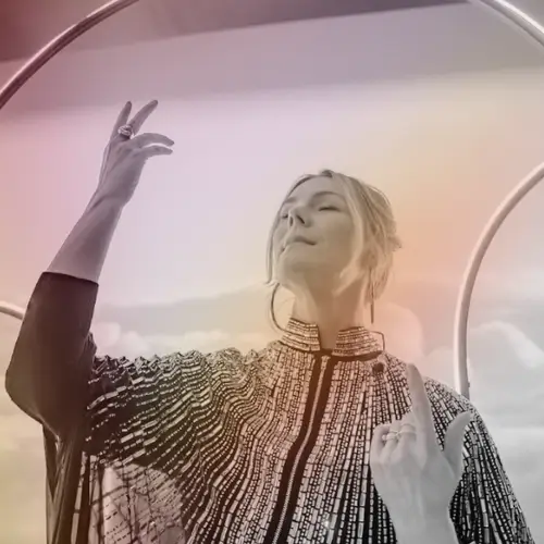 A woman in a beaded garment poses with her arms raised against a gradient background in Central Oregon.