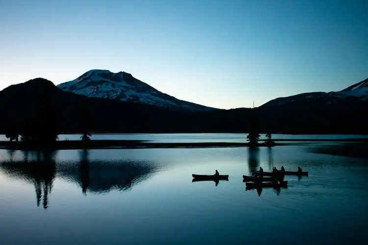 Silhouetted canoes on a calm lake at dusk with mountains in the background in Central Oregon.