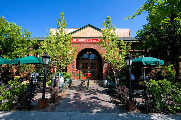 A brick building with an arched entrance and outdoor patio seating under green umbrellas in Central Oregon.