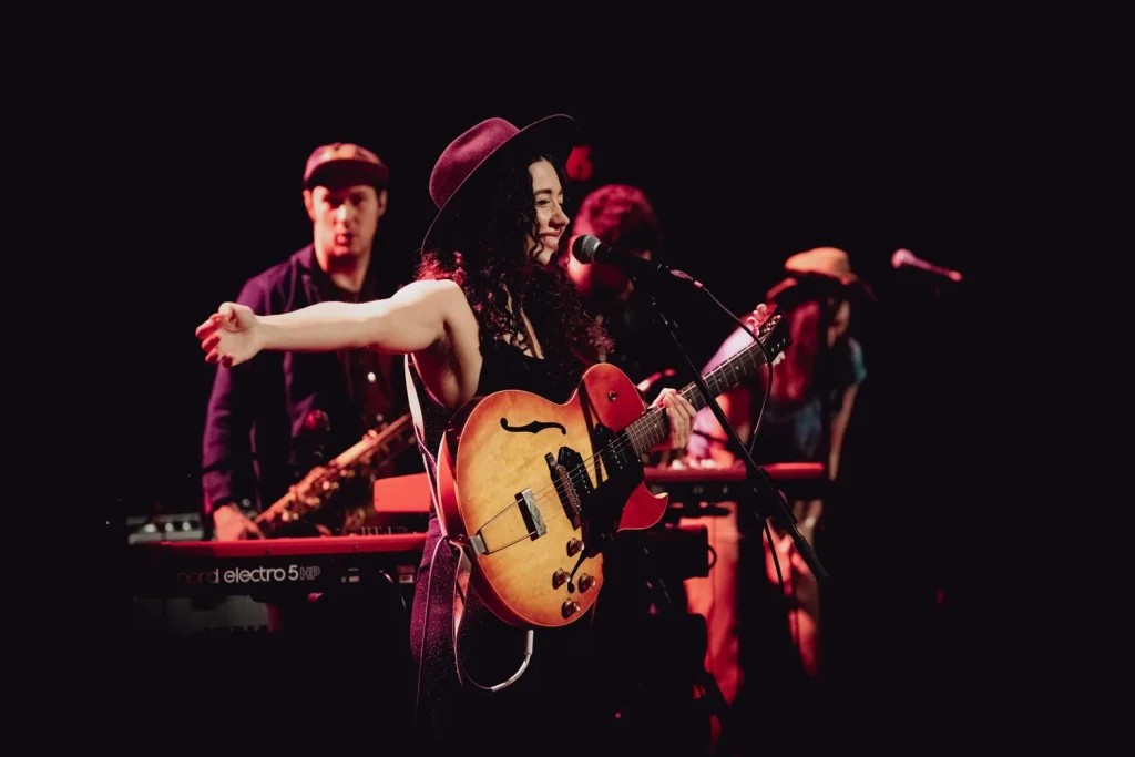 A woman in a hat plays guitar and sings on stage with her band in Central Oregon.