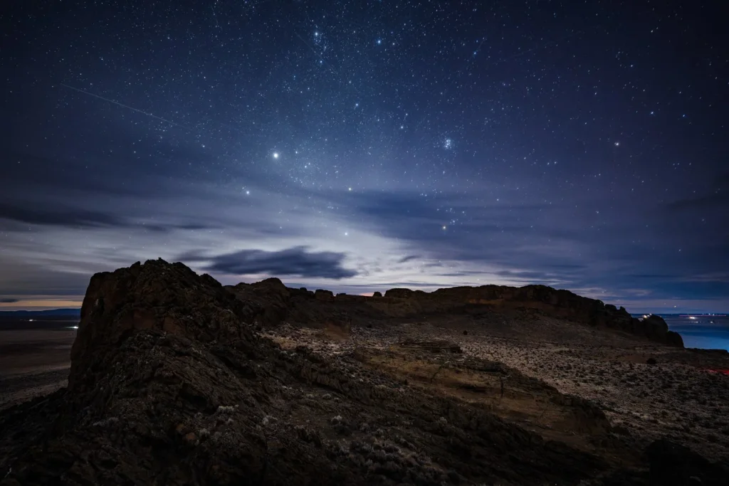 A rocky desert landscape under a vast, star-filled night sky with wispy clouds in Central Oregon.