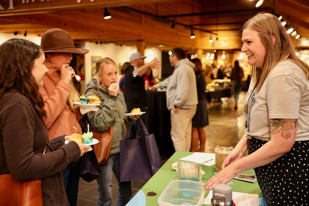 A woman smiles while talking to three people holding plates of food at an event in Central Oregon.