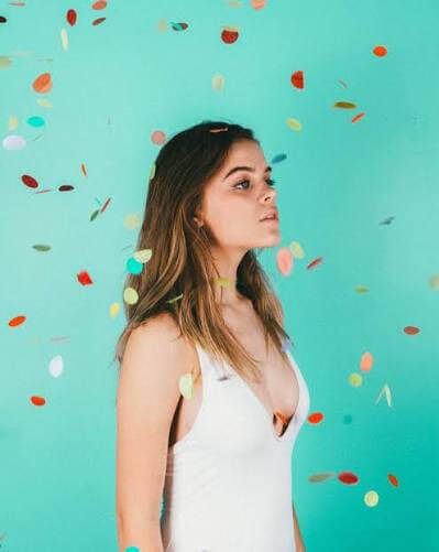 A young woman in a white top standing against a teal background with falling confetti in Central Oregon.