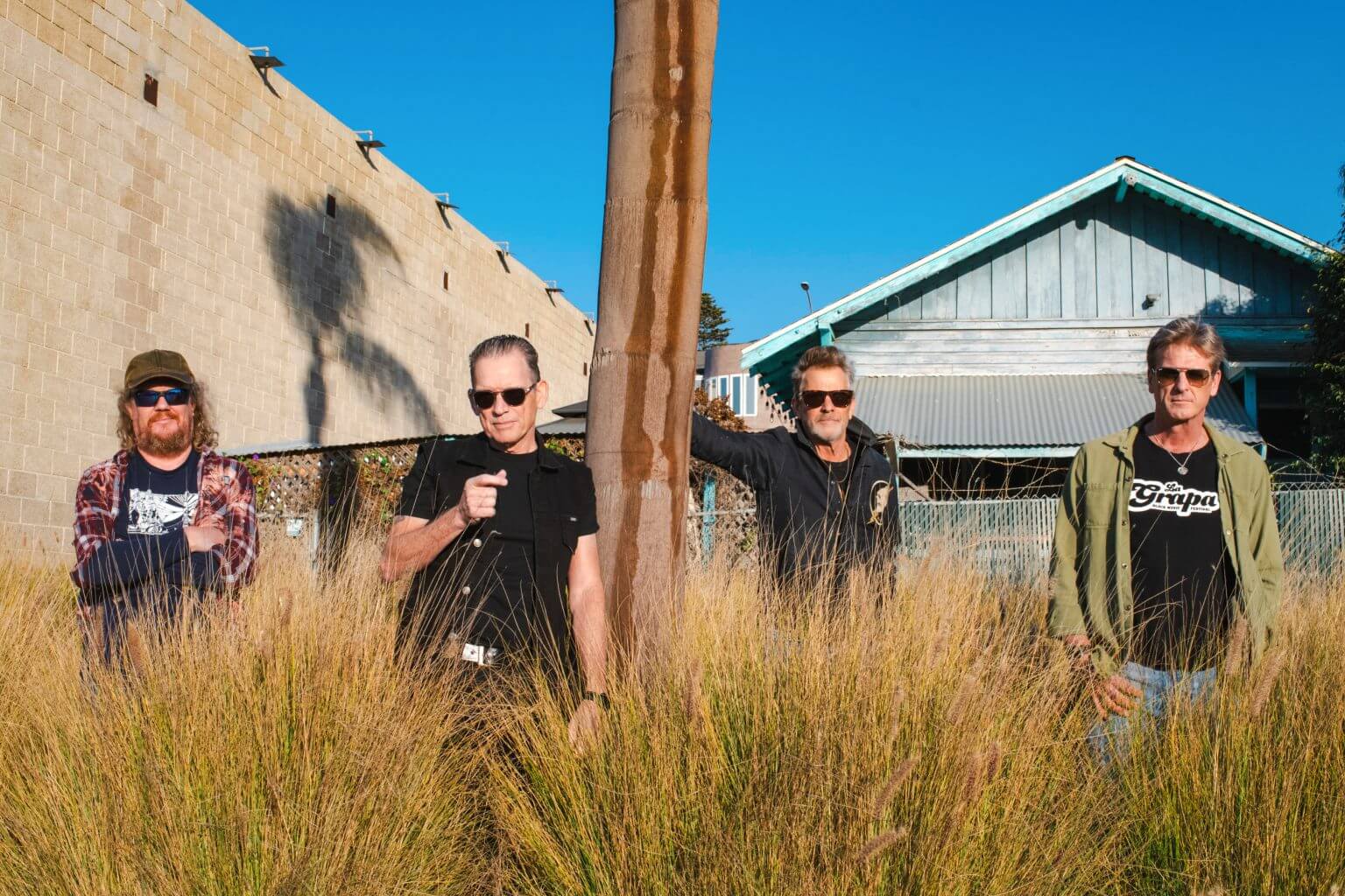 Four men wearing sunglasses stand in tall grass in front of a building in Central Oregon.