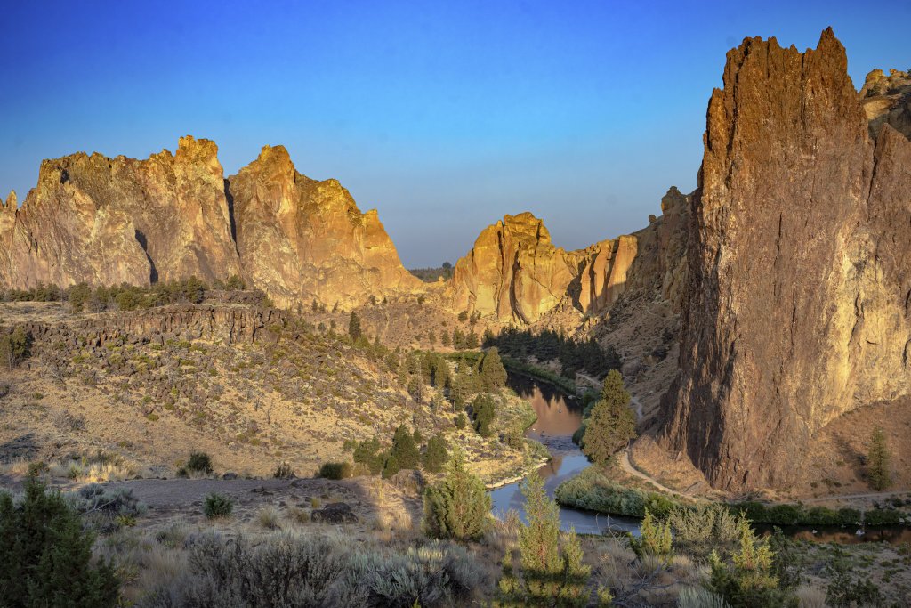 A winding river flows through a canyon with towering, sunlit rock formations in Central Oregon.