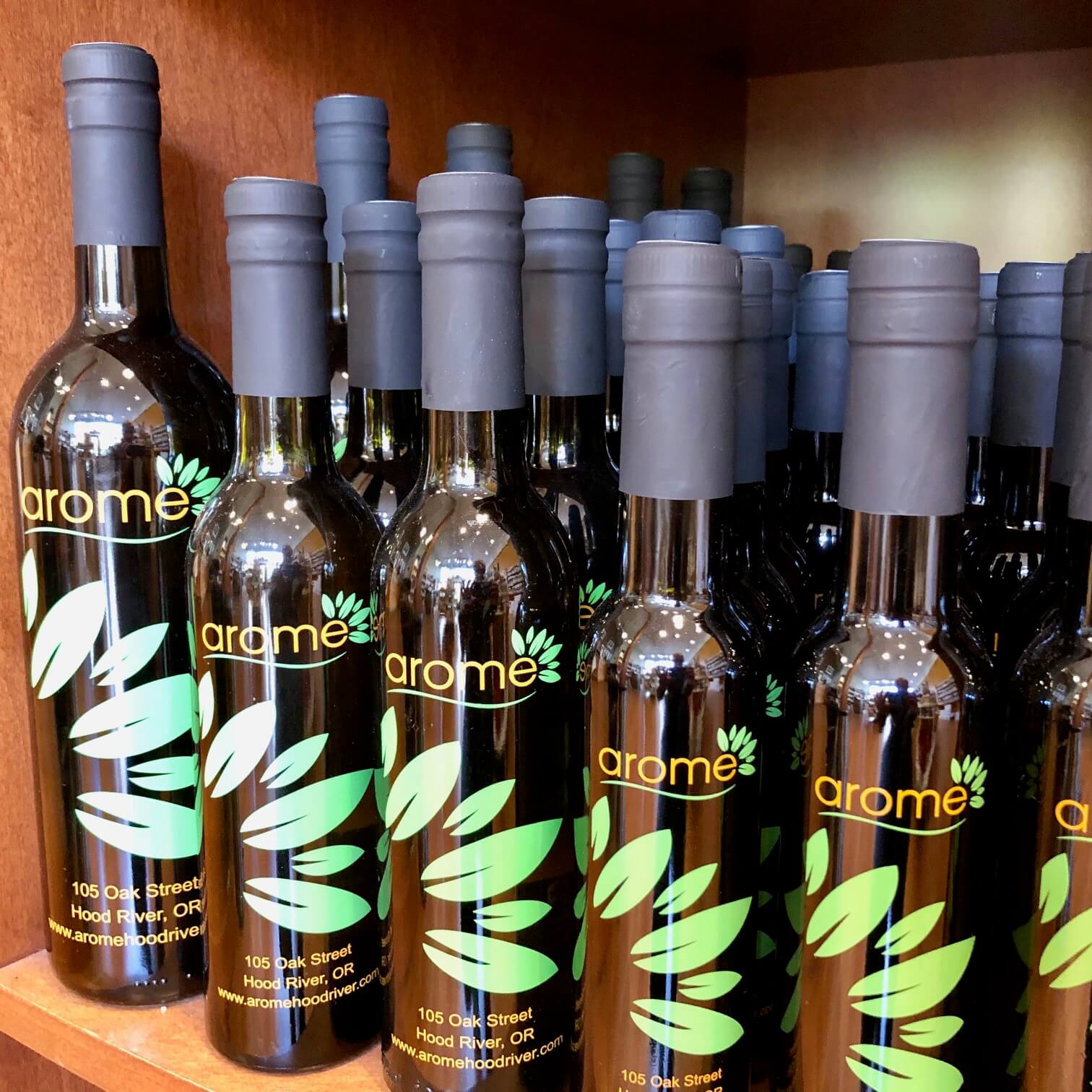Several bottles of Arome brand oil or vinegar lined up on a wooden shelf in Central Oregon.