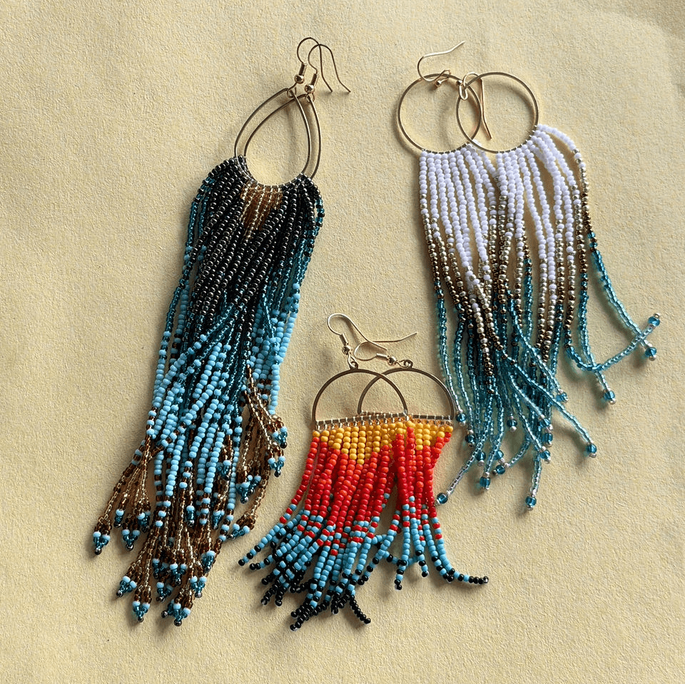 Three pairs of colorful, handcrafted beaded fringe earrings on a textured beige background in Central Oregon.