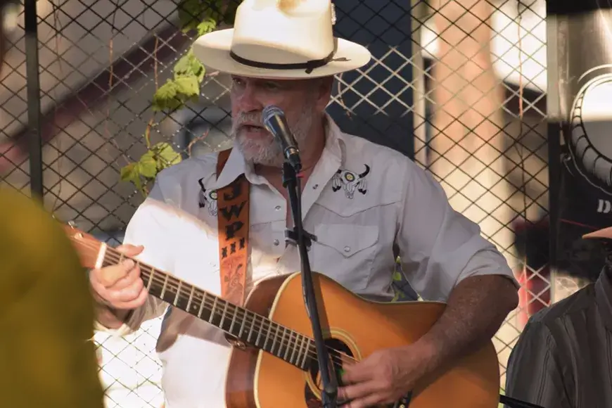 A bearded man in a cowboy hat plays acoustic guitar and sings into a microphone in Central Oregon.