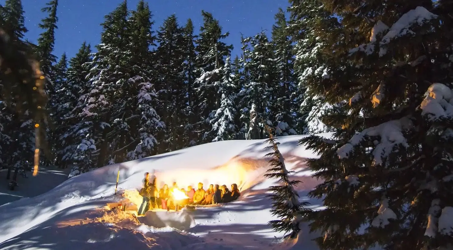A group of people gathered around a campfire in a snowy forest at night in Central Oregon.