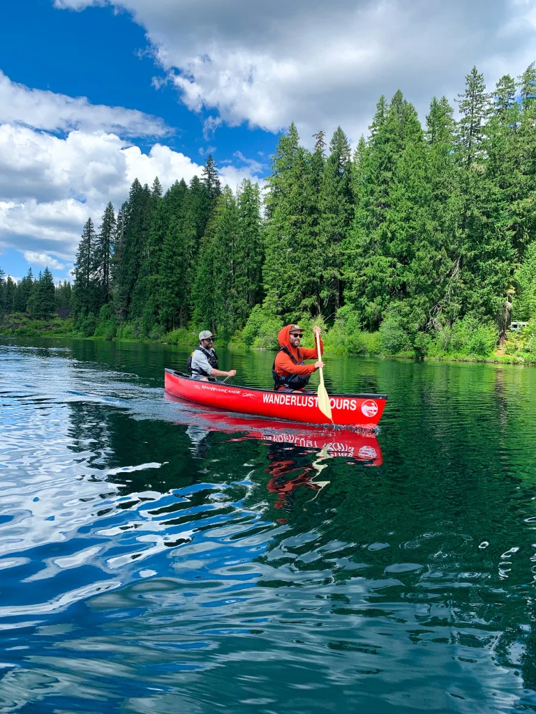 Two men paddling a red canoe on a calm lake surrounded by pine trees in Central Oregon.