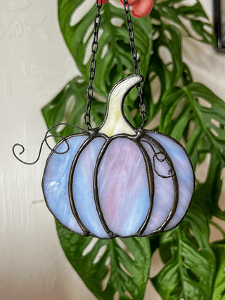 A pastel blue and purple stained glass pumpkin ornament hanging in front of leaves in Central Oregon.