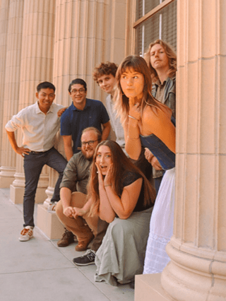 A group of seven young adults posing together near large architectural columns in Central Oregon.