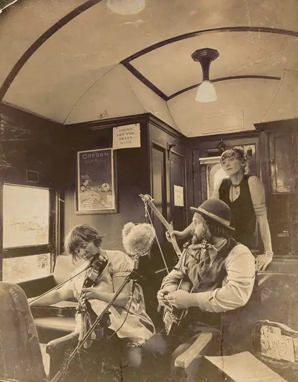 Three musicians perform inside a vintage train car in a sepia-toned photograph in Central Oregon.