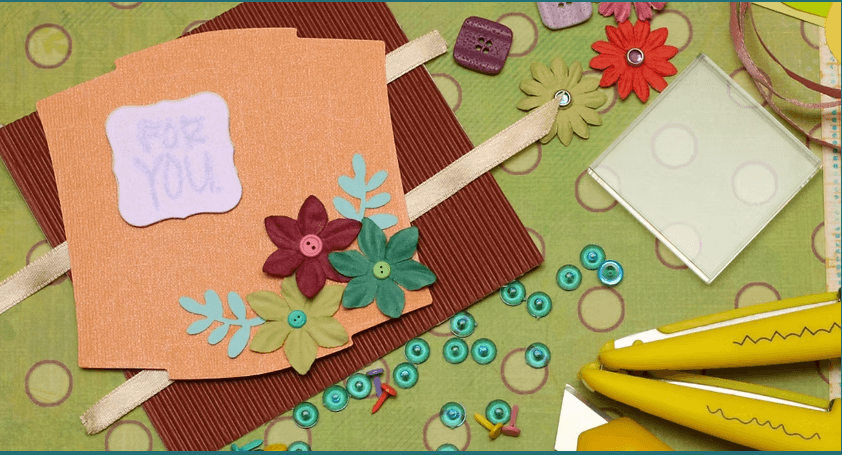 A handmade greeting card decorated with paper flowers and buttons on a craft table in Central Oregon.