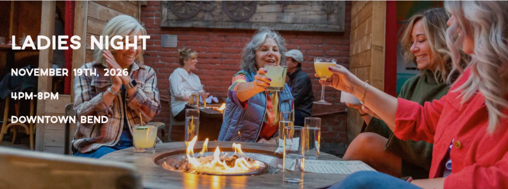 A group of women toast with cocktails around a fire pit at an outdoor event in Central Oregon.