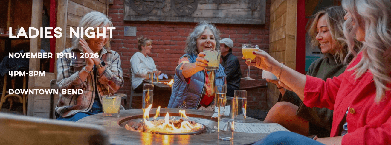 A group of women toast with cocktails around a fire pit at an outdoor event in Central Oregon.