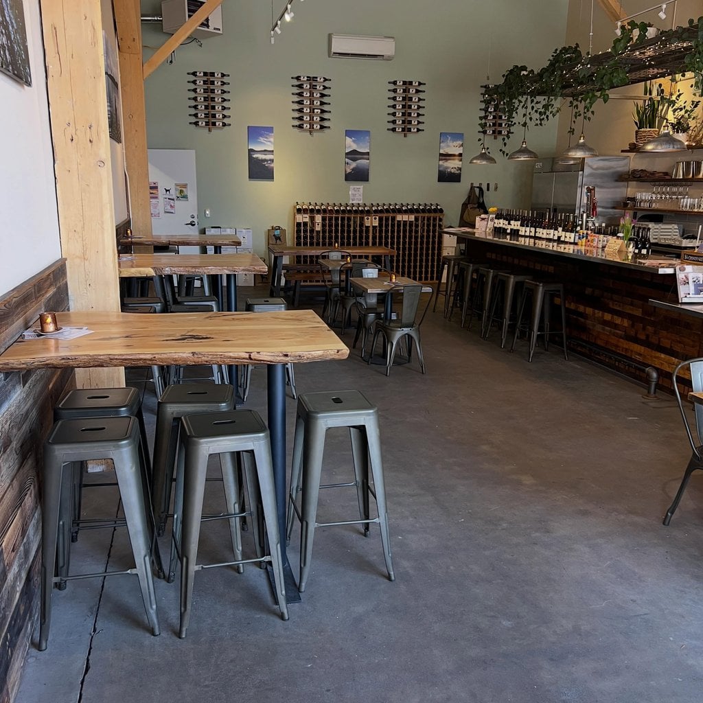 An interior view of a rustic wine bar with wooden tables and metal stools in Central Oregon.