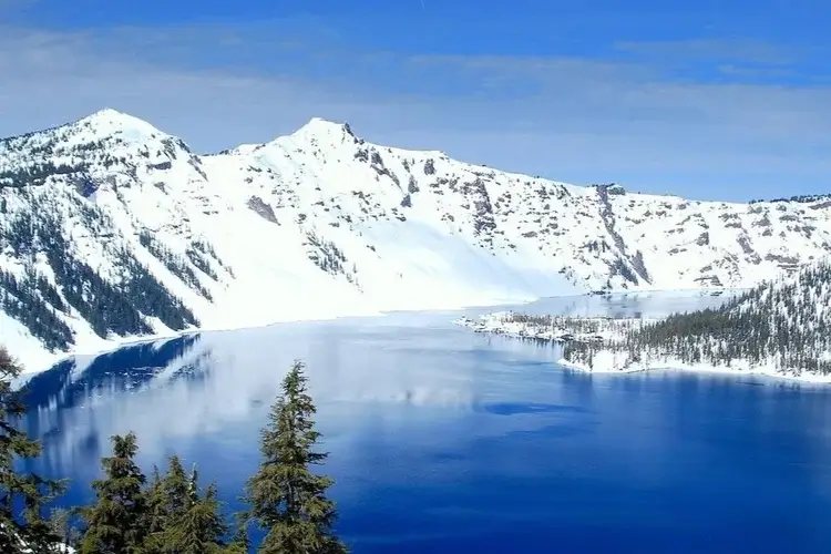 A deep blue lake surrounded by snow-covered mountains under a clear sky in Central Oregon.