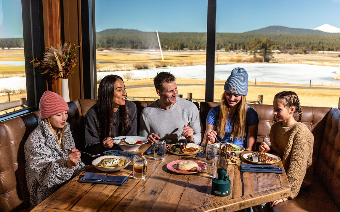 A family enjoys a meal together at a restaurant with a scenic mountain view in Central Oregon.