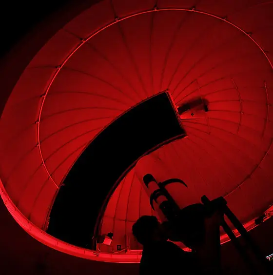 A silhouette of a person looking through a telescope inside a red-lit observatory dome in Central Oregon.