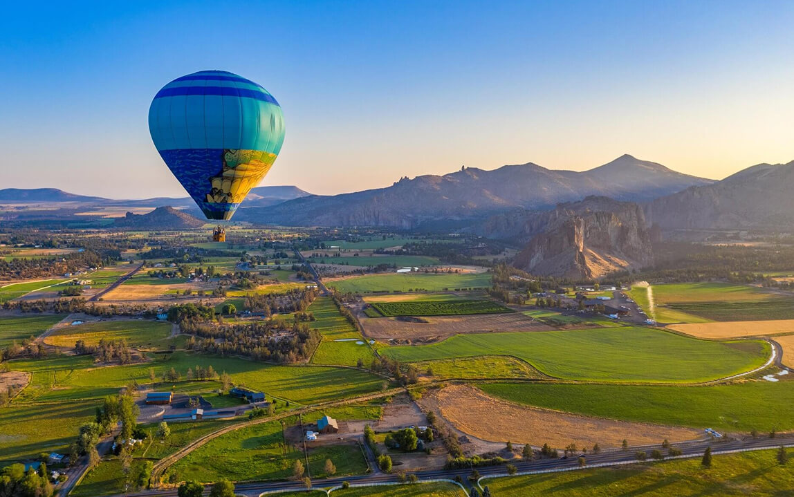 A colorful hot air balloon floats over a scenic valley at sunrise in Central Oregon.