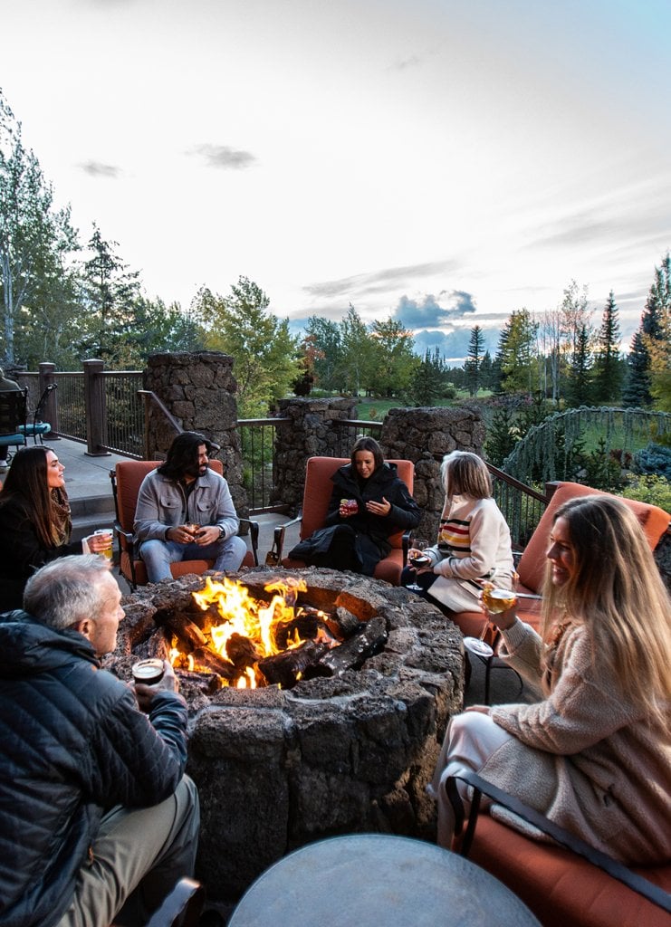 A group of friends sitting around an outdoor stone fire pit at sunset in Central Oregon.