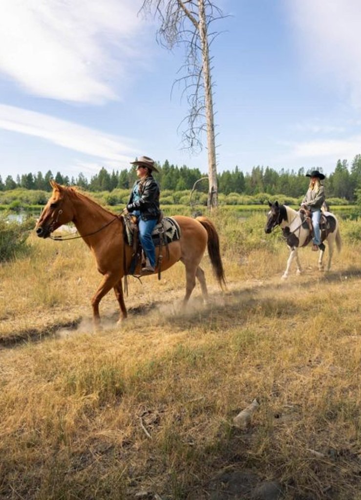 Two people wearing cowboy hats ride horses through a dry, grassy field in Central Oregon.