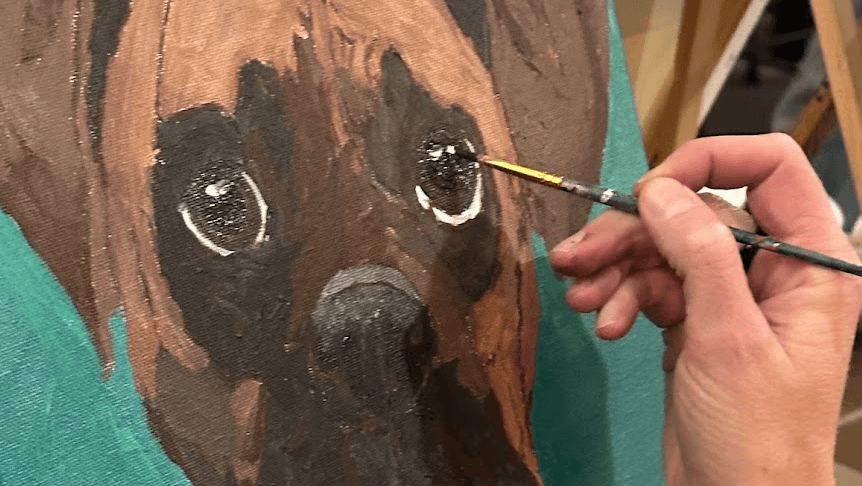 A hand uses a paintbrush to add detail to a dog painting on canvas in Central Oregon.