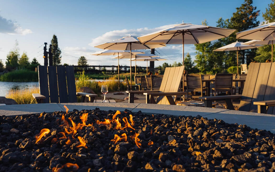 A cozy outdoor patio with a fire pit, chairs, and umbrellas overlooking a lake in Central Oregon.