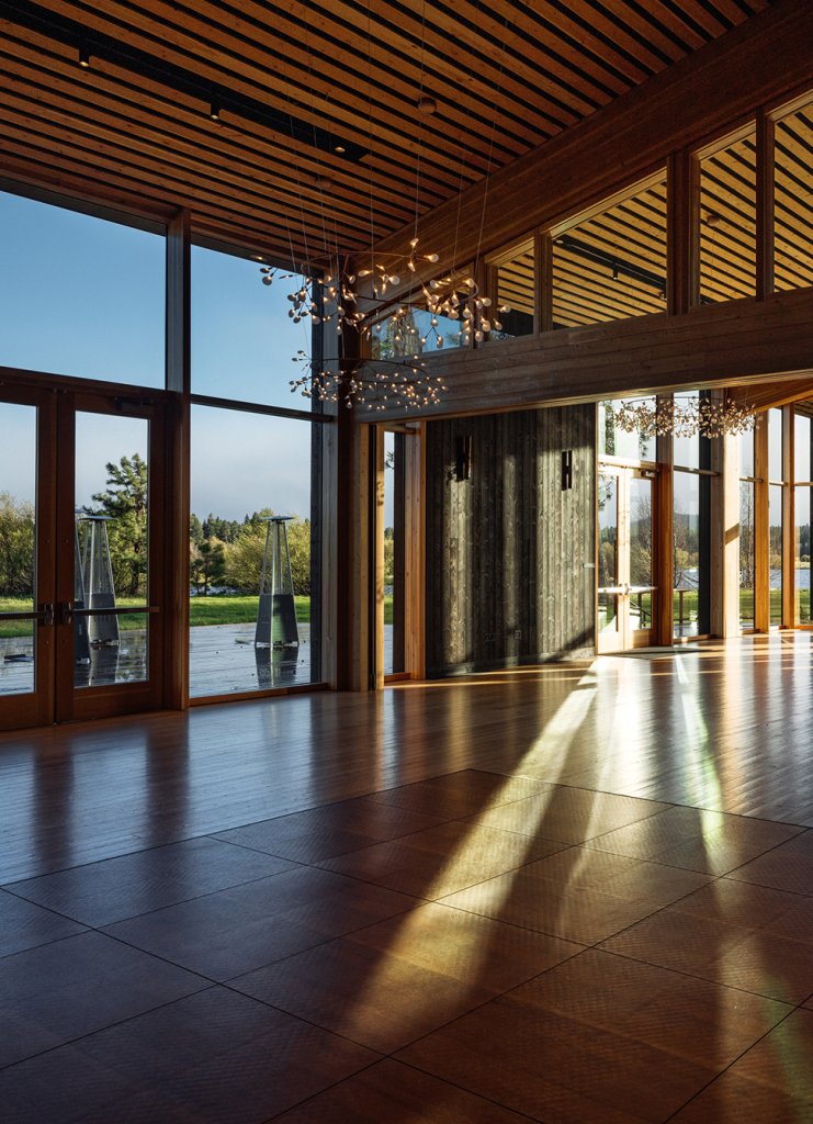 A spacious room with wooden floors, large windows, and modern chandeliers overlooking a landscape in Central Oregon.