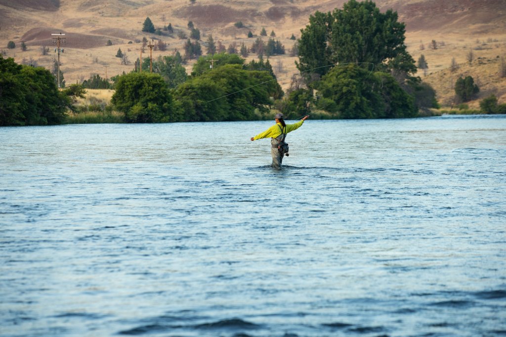A person fly fishing in a river with hills in the background in Central Oregon.