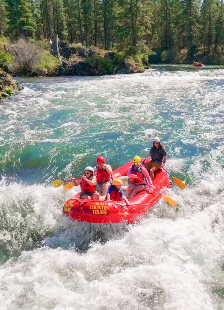 A group of people in a red raft navigating river rapids in Central Oregon.