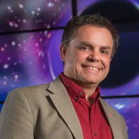 A smiling man wearing a red shirt and tan blazer against a purple background in Central Oregon.