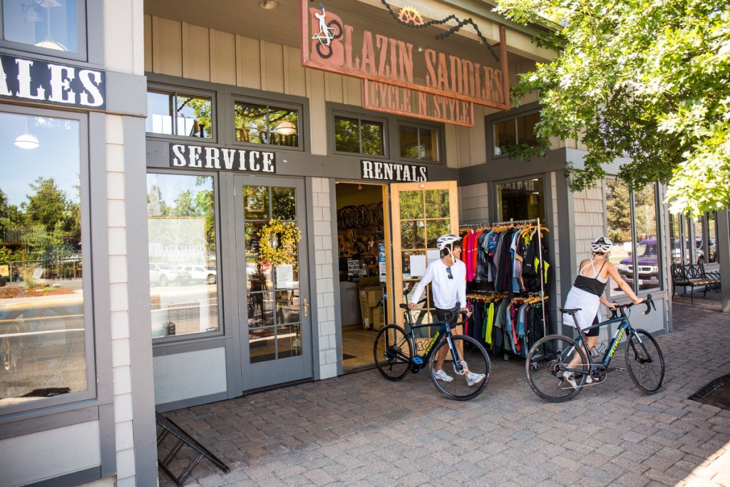 Two cyclists with helmets standing outside a bike shop called Blazin Saddles in Central Oregon.