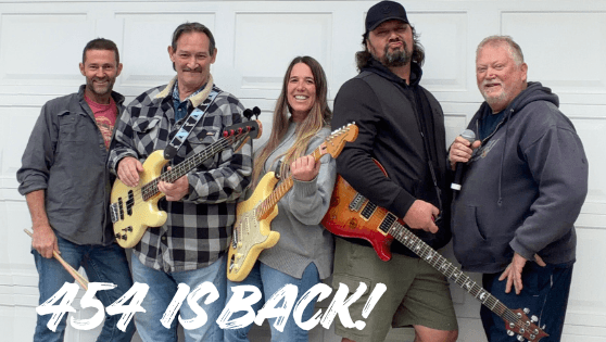 A five-member band poses together with musical instruments in front of a white garage door in Central Oregon.