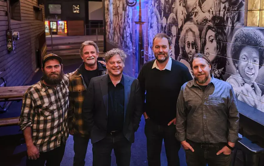 Five men standing together in an alleyway with a mural on the wall in Central Oregon.
