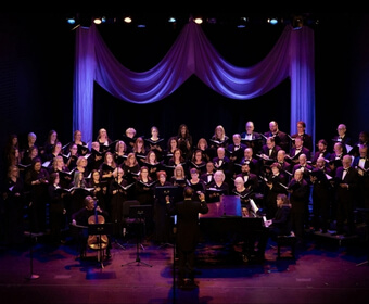 A large choir performing on a stage with a conductor and musicians in Central Oregon.
