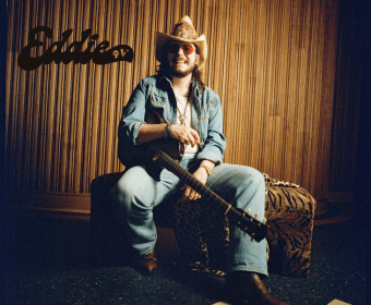 A man in a cowboy hat and denim shirt holding an acoustic guitar in Central Oregon.
