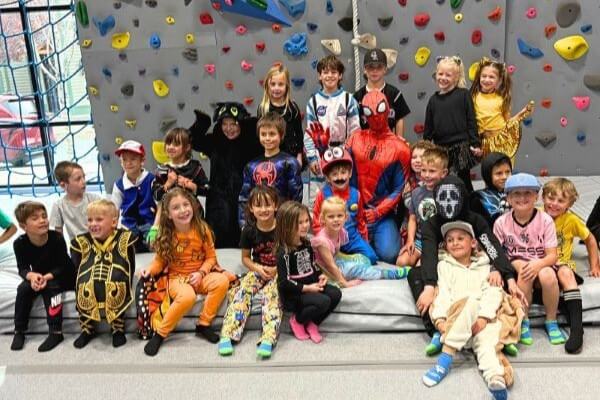 A large group of children in costumes posing in front of an indoor climbing wall in Central Oregon.